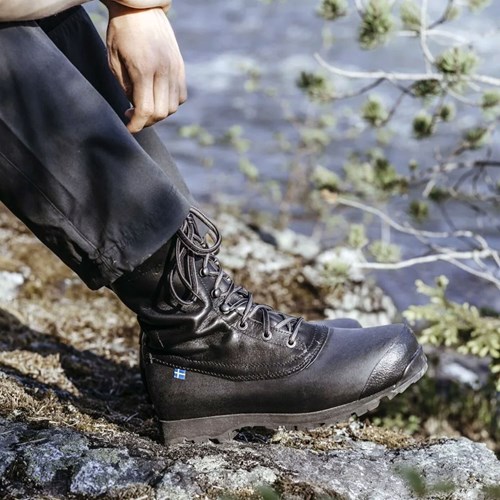 A person&#39;s feet in black boots on a rock.