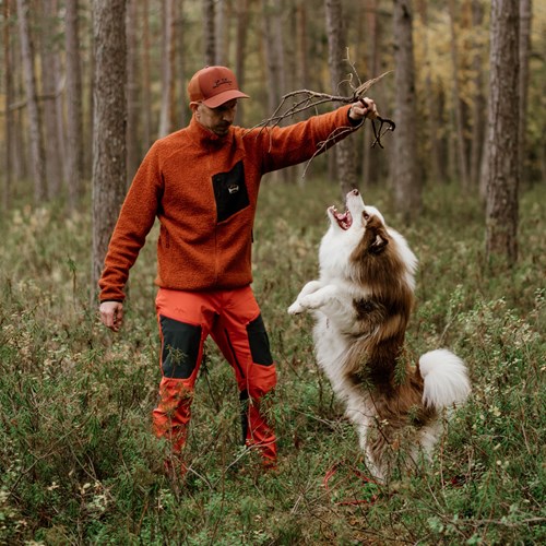 En mann som holder en pistol og en hund i en skog.