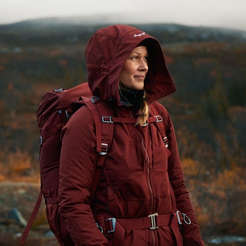 A person wearing a red coat and a hoodie standing in front of a forest.
