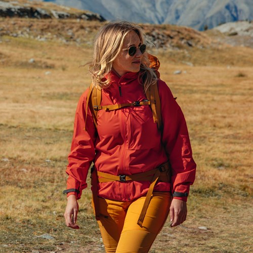 A person wearing a red coat and sunglasses walking in a field.