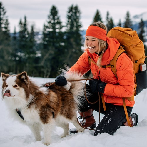 A person in orange jacket and dog in the snow.