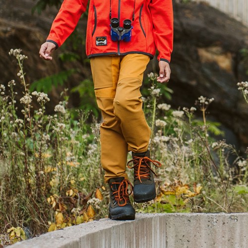 A person wearing a red jacket and yellow pants standing on a ledge.
