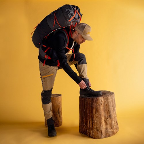 A person wearing a backpack and standing on a stump.
