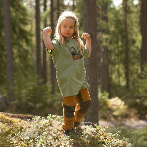 A girl in a green shirt and yellow pants running in the woods.