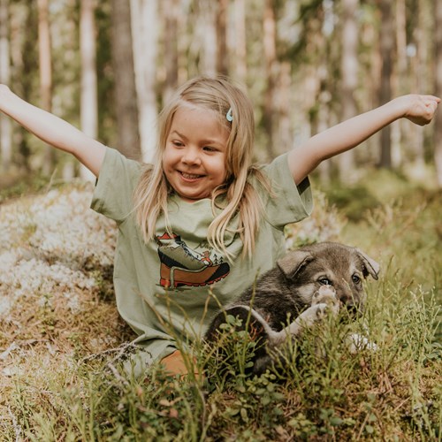 A girl with her arms out and a deer in the grass.